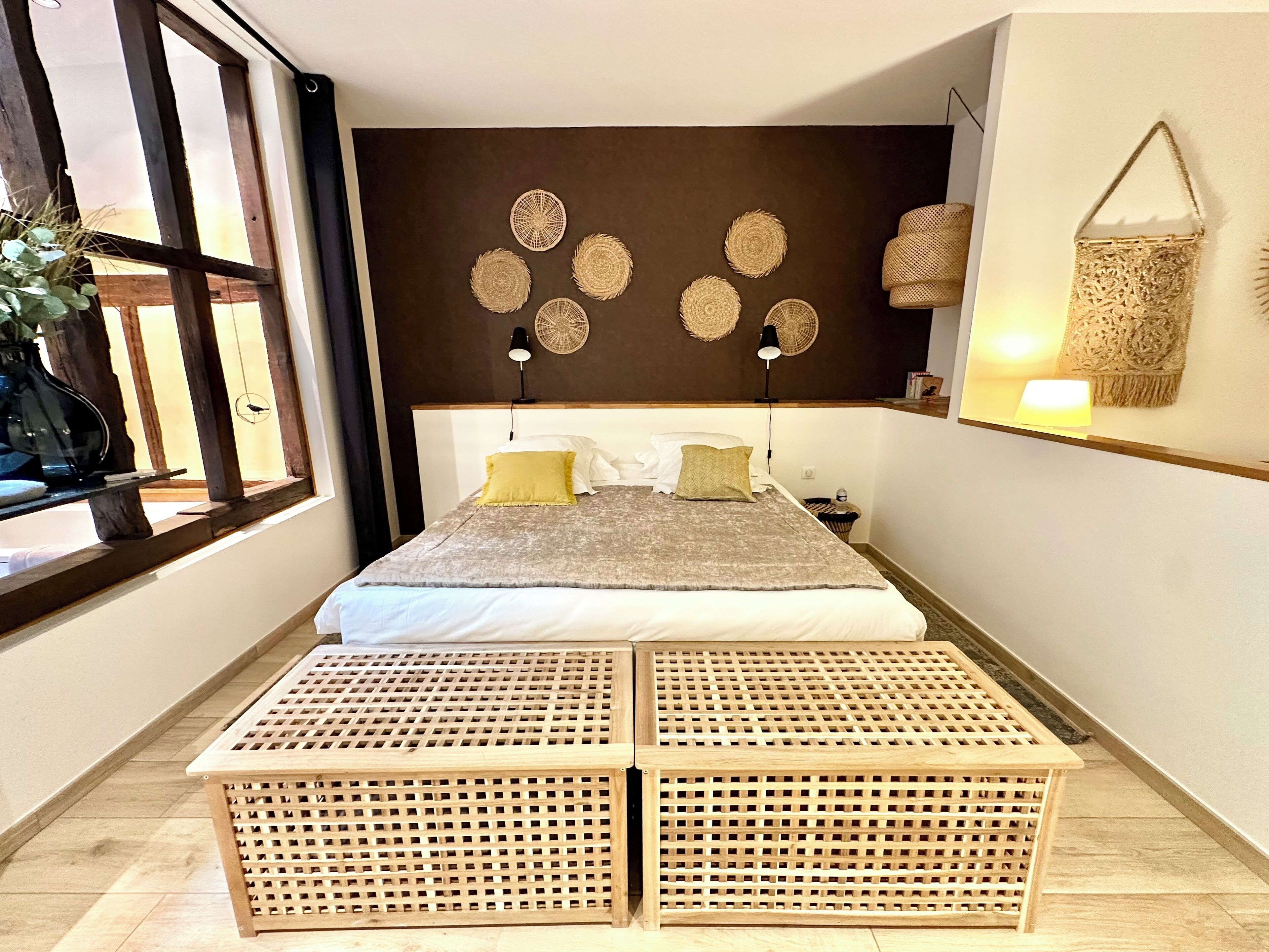 Un dormitorio con cama, lámparas de noche, un adorno tejido en la pared y una ventana con vistas.