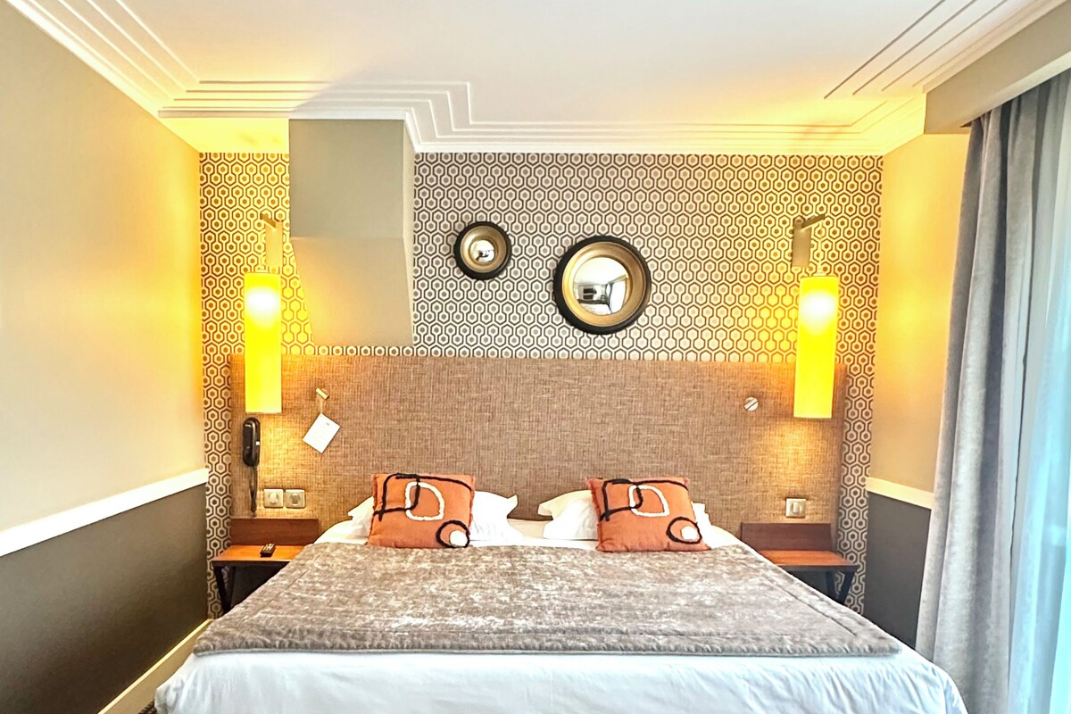 A hotel room with a large bed, two bedside tables, a headboard with a mirror, and patterned walls.