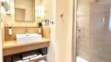 A modern bathroom with a large sink, mirror, and a glass-enclosed shower.