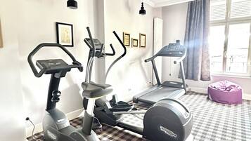 A home gym with two treadmills and an elliptical machine, a patterned carpet, a purple bean bag, and a window with curtains.