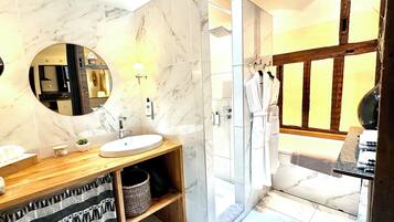 A bathroom with a marble vanity, a sink, a mirror, a shower, and a wooden door.