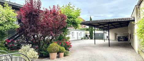 A gravel courtyard with a covered seating area, a white building, and a tree with red leaves.