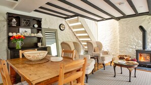 A cozy living room with a wooden dining table, comfortable chairs, a fireplace, and a staircase leading to another level. - Cottage in Nannau Estate Near Coed Y Brenin (Dolgellau)