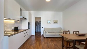 Eine moderne Küche mit weißen Schränken und einer Holz Arbeitsplatte, ein beiges Sofa und ein Esstisch mit Stühlen.