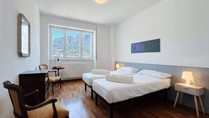 Ein Schlafzimmer mit zwei Betten, einem Schreibtisch, einem Sessel, einem Nachttisch und einem Fenster mit Blick auf die Berge.