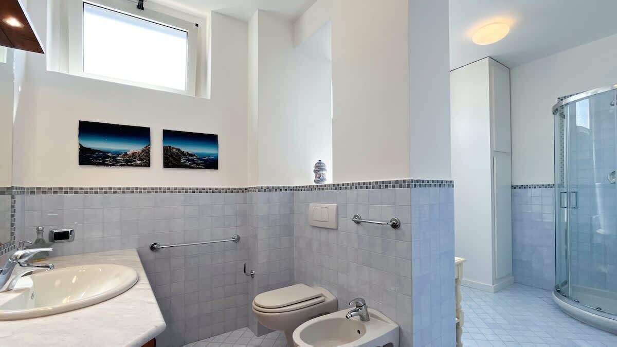 A modern bathroom with a large sink, toilet, bidet, and glass shower enclosure.