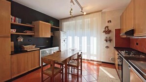 A modern kitchen with wooden cabinets, a dining table, and a large window with sheer curtains. - Welcome House - Affitti Brevi italia (Lecco)