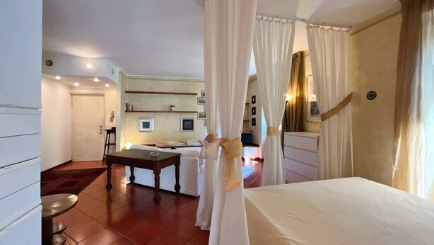 A hotel room with a bed, a desk, and a chair. There is a curtain in the doorway. - Welcome House - Affitti Brevi italia (Lecco)