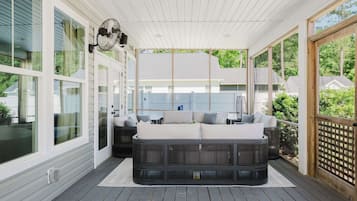 A covered porch with a sectional sofa, a ceiling fan, and large windows.