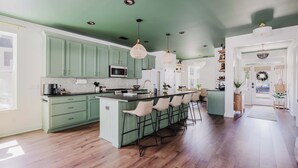 Une cuisine avec des meubles de couleur verte, un îlot central doté de tabourets et des luminaires suspendus.