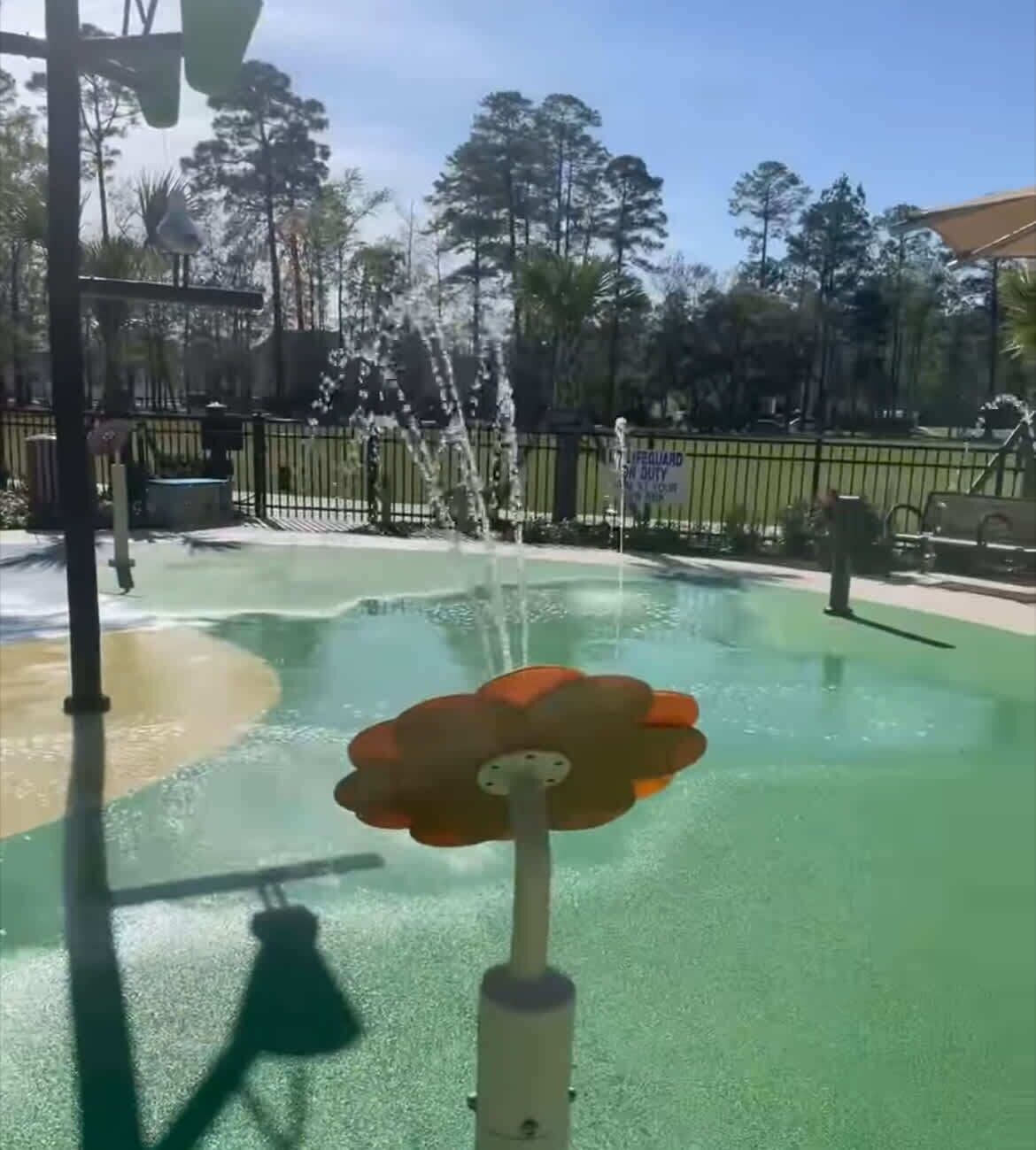 Ein Wasserspiel mit einer blumenförmigen Struktur in einer parkähnlichen Umgebung.