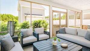 A covered outdoor seating area with sofas and a coffee table, large windows, and a view of greenery.
