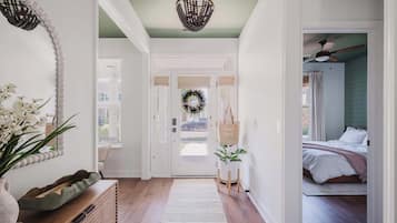 A hallway with a wooden bench, a decorative wall piece, a chandelier, and a bed in the adjacent room.
