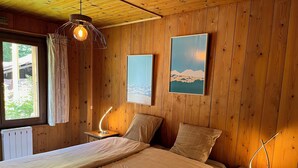 A wooden-paneled room with a bed, a nightstand with a lamp, a window with curtains, and a painting on the wall. - Appartment 4 persons in Morzine (Morzine)