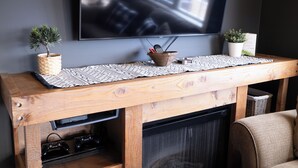 Un meuble de rangement en bois pour appareils électroniques, avec un téléviseur fixé au-dessus, une petite plante en pot et un set de table en fibres tressées.