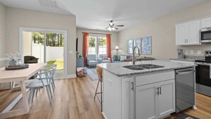 Een moderne keuken met een centraal eiland, witte kasten en een eethoek met tafel en stoelen.