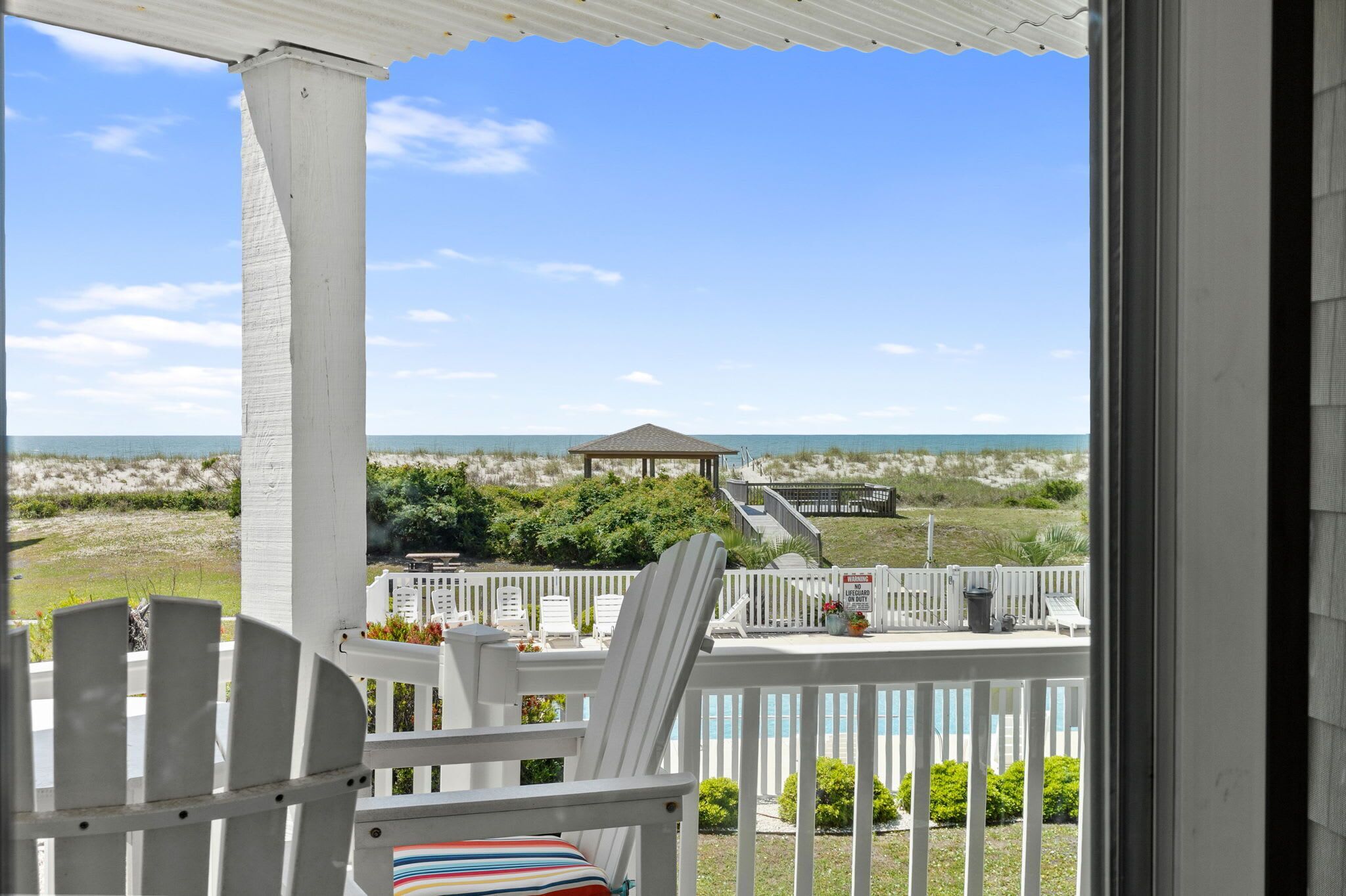 A balcony with white railings, a white chair, and a view of the beach and ocean.