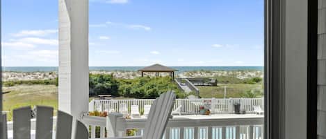 A balcony with white railings, a white chair, and a view of the beach and ocean.