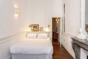 A hotel room with a large bed, a marble fireplace, and a mirror.