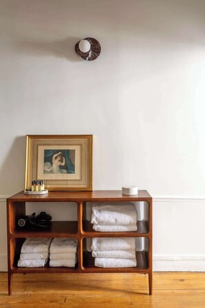 A wooden shelf with folded towels, a framed artwork, and a small white object on top.