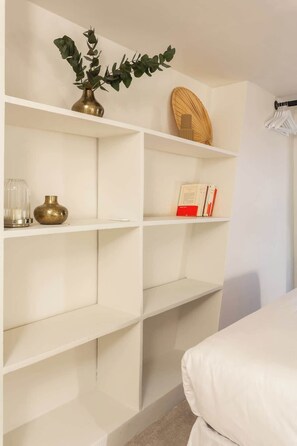Habitación minimalista con estanterías blancas, una cama y una pequeña planta.