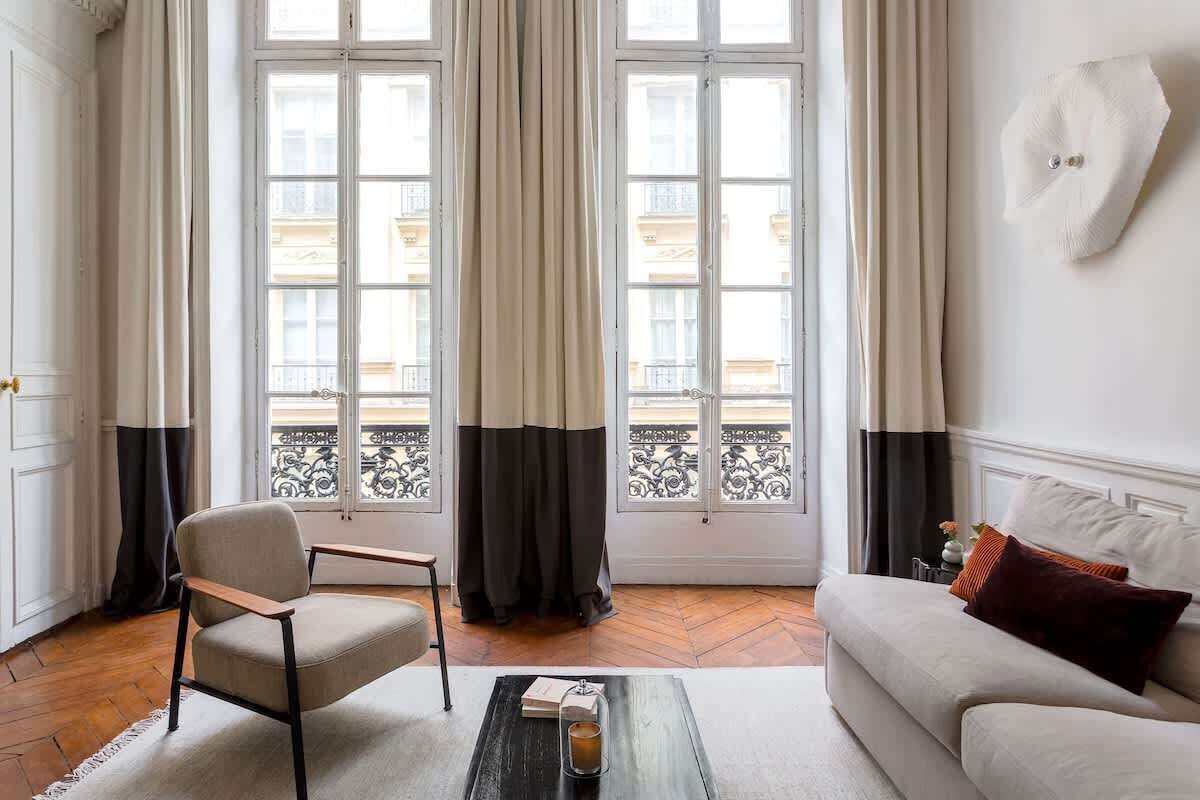 Ein Zimmer mit einer Couch, einem Sessel, einem Couchtisch und einem Fenster mit Vorhängen.
