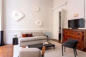 Una sala de estar moderna con un sofá, una mesa de centro y sillas. Hay un televisor sobre un mueble de madera y decoración artística en la pared.