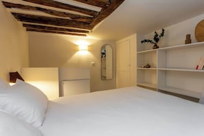 A bedroom with a bed, a mirror, a shelf with decorative items, and a wooden ceiling.