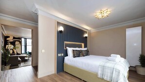 Une chambre moderne avec un grand lit, une tête de lit dotée d’un éclairage intégré, une table de chevet et une plante en pot.