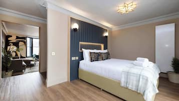 A modern bedroom with a large bed, a headboard with built-in lighting, a bedside table, and a potted plant.