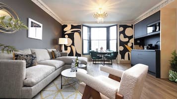 A modern living room with a sofa, armchairs, a dining table, and a kitchen area.