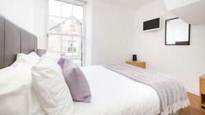 A modern bedroom with a large bed, a window, a flat-screen TV, and a small bedside table.