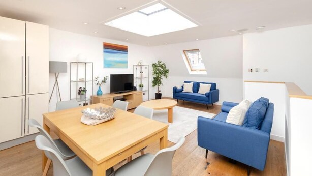 A modern living room with a wooden dining table, blue sofa, and a TV.