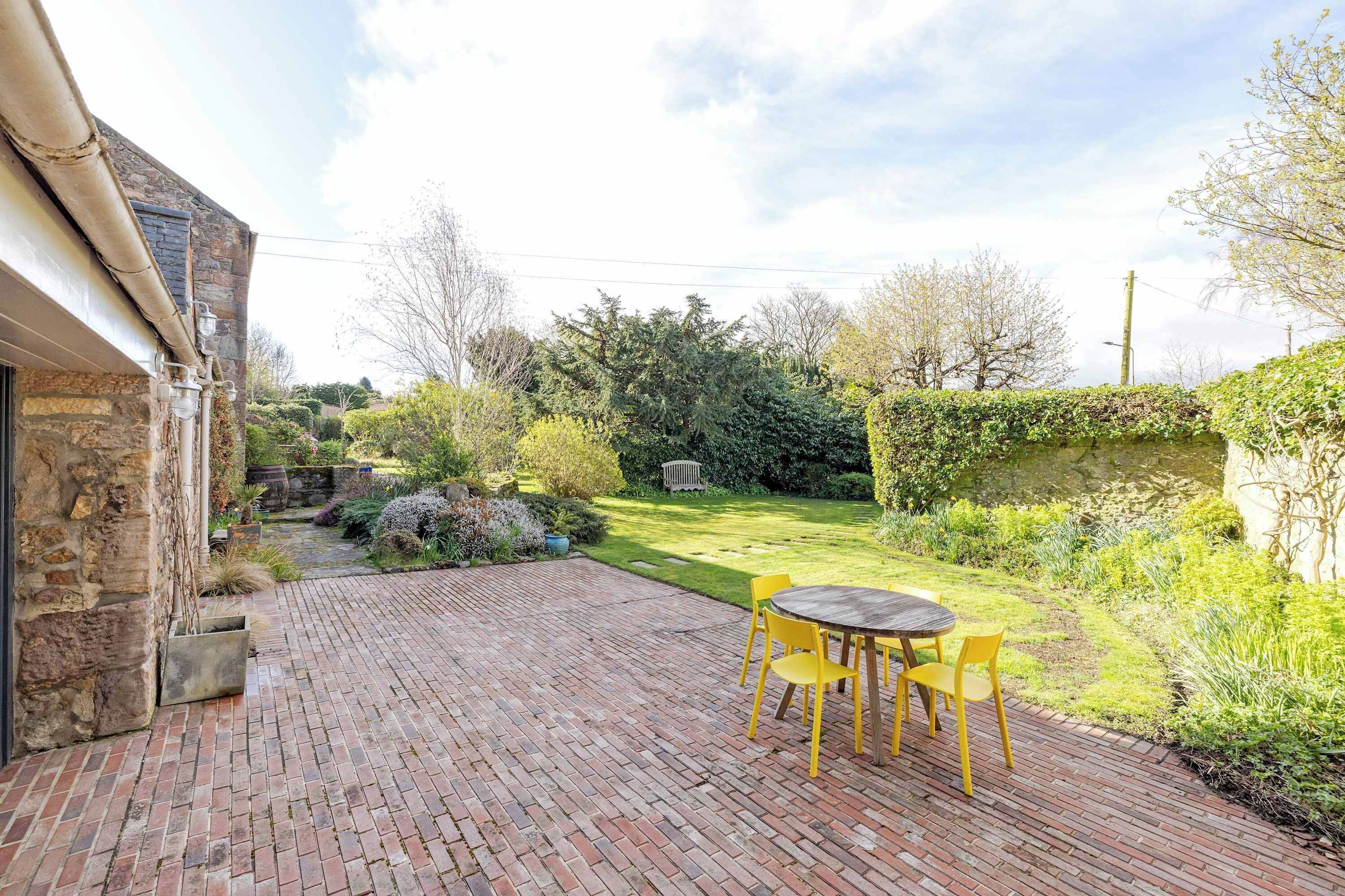 A patio with a brick floor, a round table, and yellow chairs.