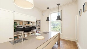 A modern kitchen with white cabinetry, a central island, pendant lighting, and a view through a window.