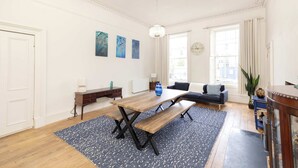 A spacious living room with a wooden dining table, a sofa, and a large window with curtains.