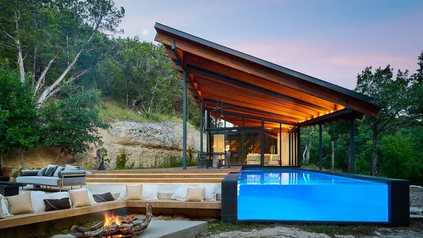Un área de piscina moderna al aire libre con terraza de madera, asientos y un hogar para fuego.