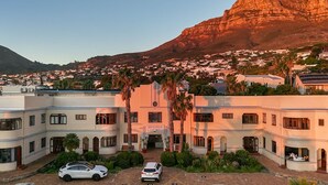 A hotel with a central entrance, surrounded by palm trees and a mountainous backdrop.