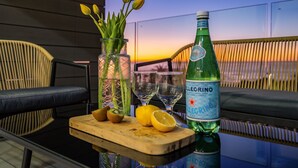 A table with a bottle of liquor, glasses, a cutting board with fruit, and a vase with flowers.