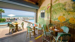 Un restaurant situé en bord de mer, doté d’une terrasse, d’une piscine et orné d’une fresque représentant des fleurs tropicales et des palmiers.