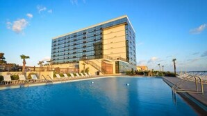 Un hôtel moderne doté d’une grande piscine, de chaises longues et offrant une vue sur l’océan.