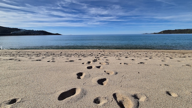 A beach with footprints in the sand and a clear sky.