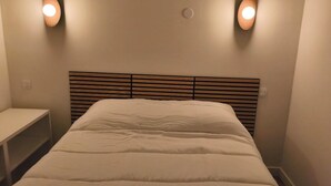 A neatly made bed with a wooden headboard, two wall-mounted lights, and a small bedside table. - Apartment with pool at the foot of the slopes (Flumet)