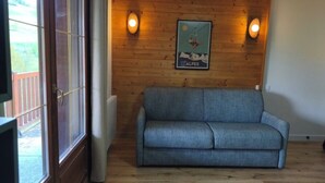 A room with a wooden wall, a grey sofa, and a poster of a skier. - Apartment with pool at the foot of the slopes (Flumet)
