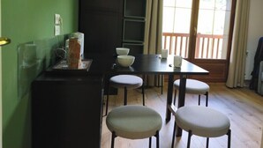 A compact kitchen with a dining table and four chairs, a small refrigerator, and a window with a view of a wooden deck. - Apartment with pool at the foot of the slopes (Flumet)