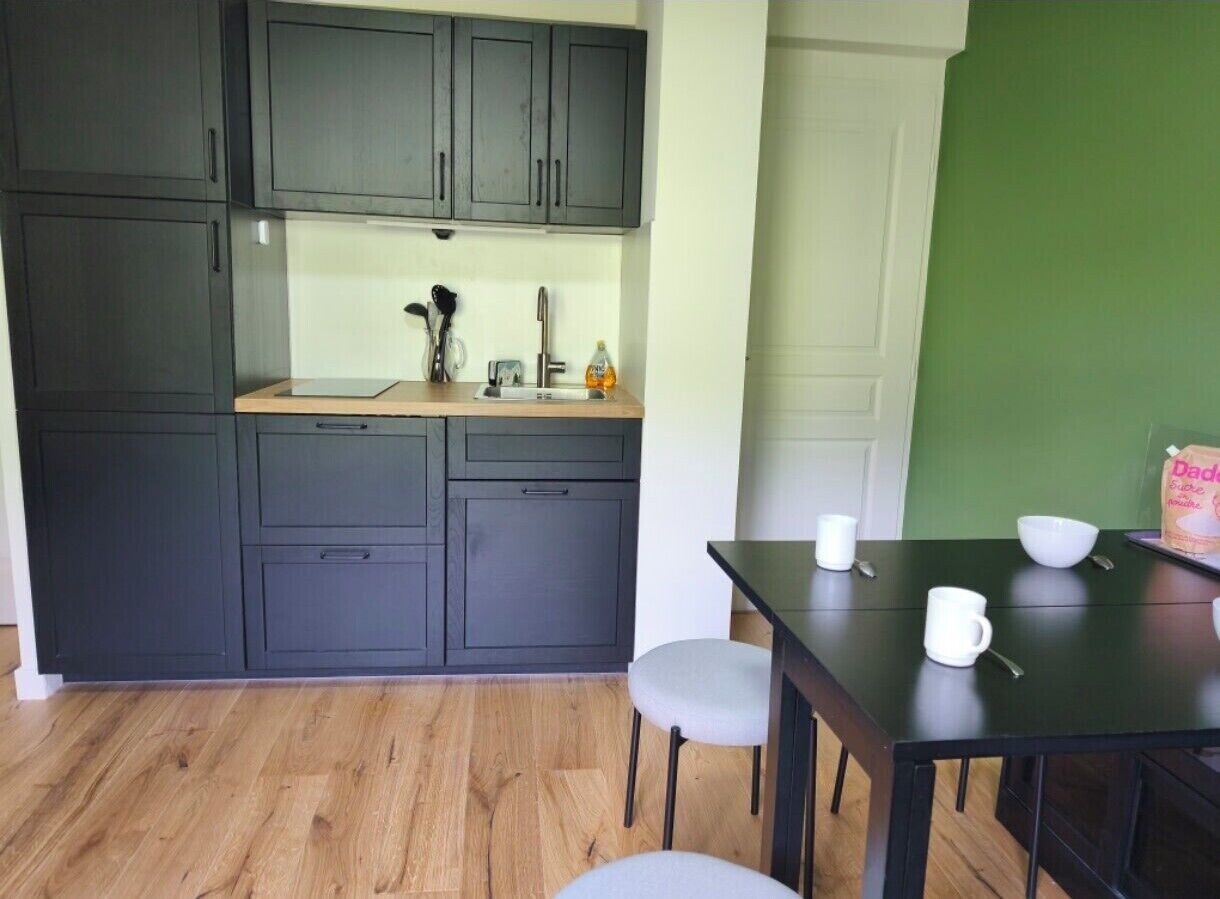 Cocina compacta con armarios oscuros, encimera de madera y zona de comedor con mesa y sillas.