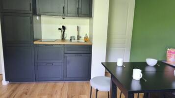 Cocina compacta con armarios oscuros, encimera de madera y zona de comedor con mesa y sillas.