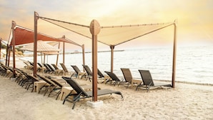A beach with rows of sun loungers and umbrellas, a wooden structure, and the ocean in the background. - Signature Blue Resort (Kuşadası)