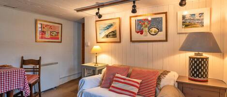 Una camera accogliente con un letto, un tavolo, sedie, una lampada e quadri appesi al muro.