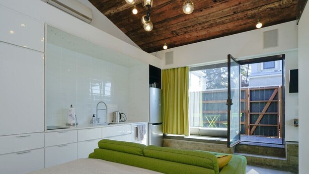 A modern bedroom with a large bed, a built-in wardrobe, a window with a view, and a wooden ceiling.
